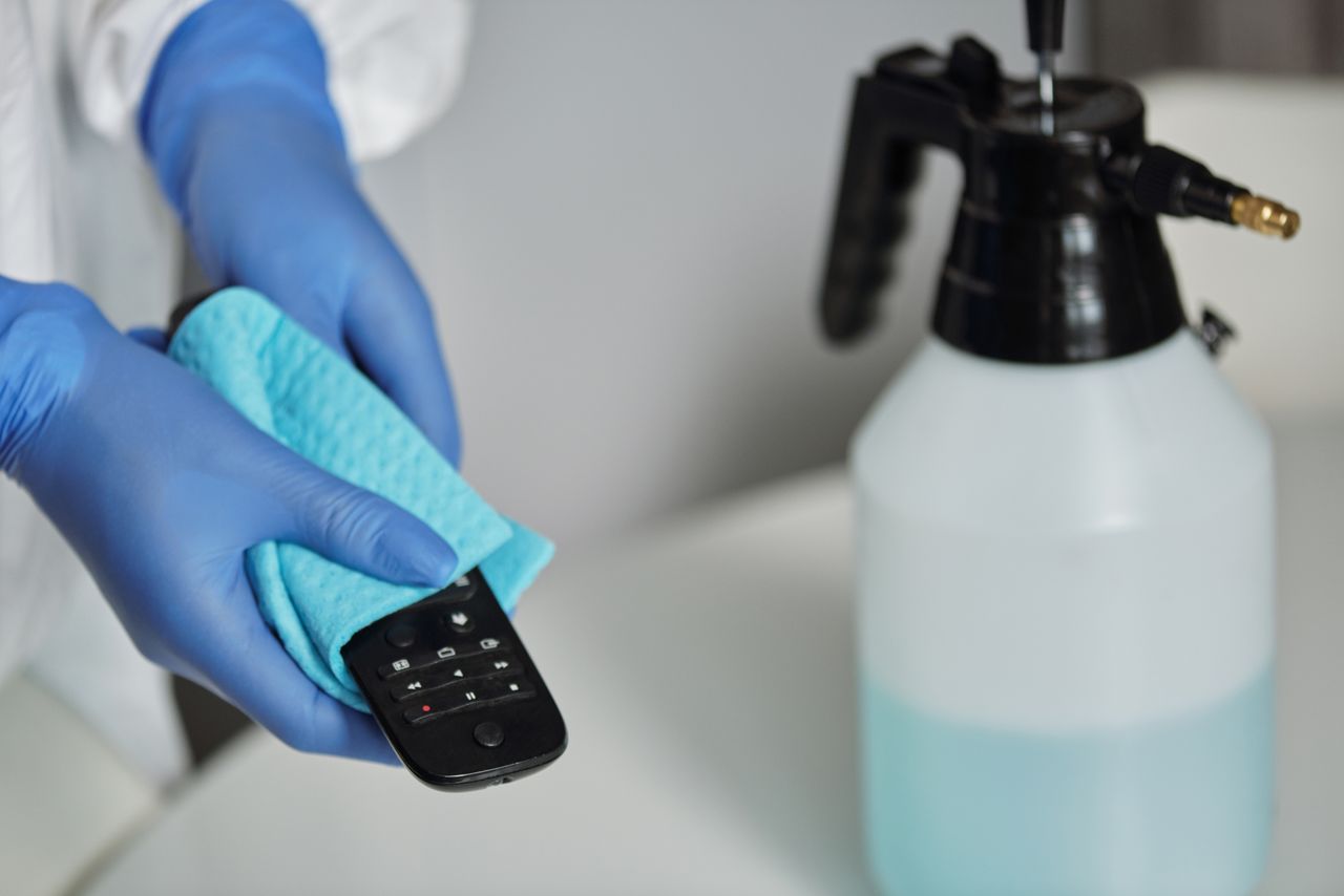 creative Close-up of gloved hands disinfecting a remote control with a cloth and spray bottle.