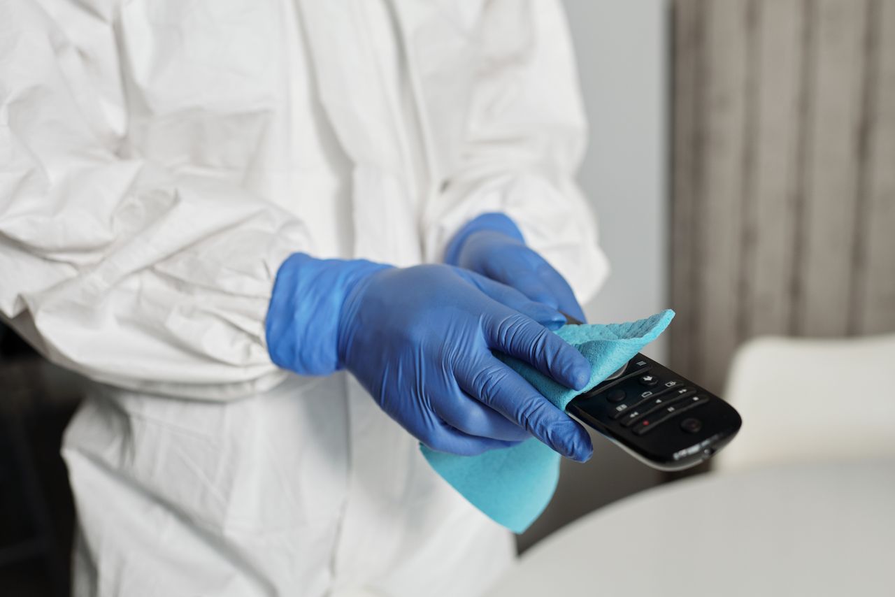 mobile-01 Close-up of a person disinfecting a remote control wearing protective gloves, ensuring cleanliness.