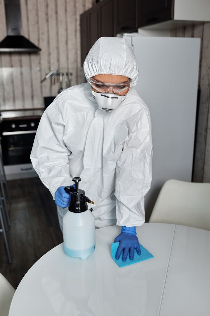 digital-01 A person in full PPE disinfecting a table indoors for hygiene and safety.